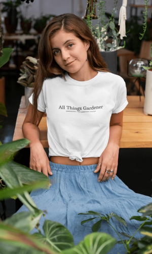 Knotted-t-shirt-mockup-of-a-woman-at-a-table-surrounded-by-plants-27083